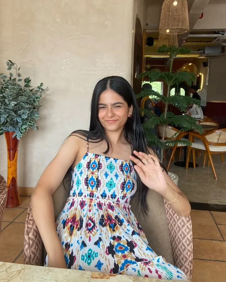 Himanshi smiling in a patterned dress, seated in a café