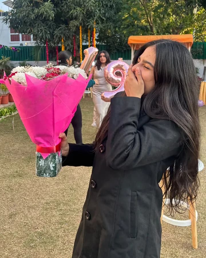 Himanshi laughing behind a pink bouquet