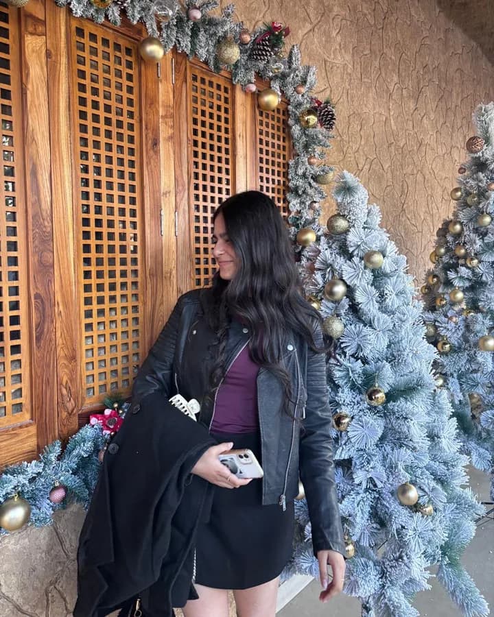 Himanshi in a leather jacket beside a Christmas tree